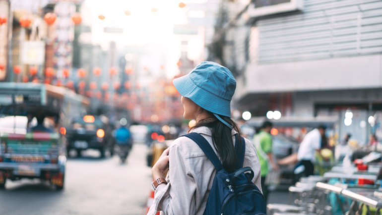 Rear view of walking young adult asian woman traveller backpack