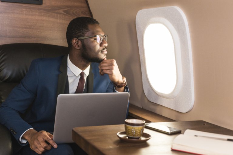 Attractive and successful African American businessman with glasses working on a laptop while sitting in the chair of his private jet.