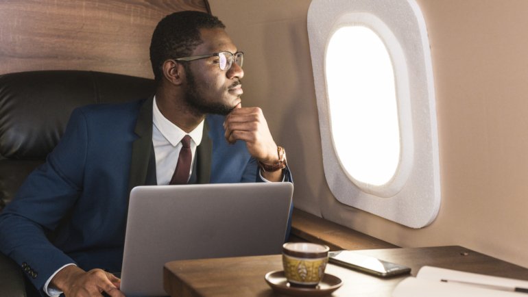 Attractive and successful African American businessman with glasses working on a laptop while sitting in the chair of his private jet.