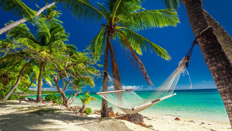 Empty hammock in the shade of palm trees on tropical Fiji