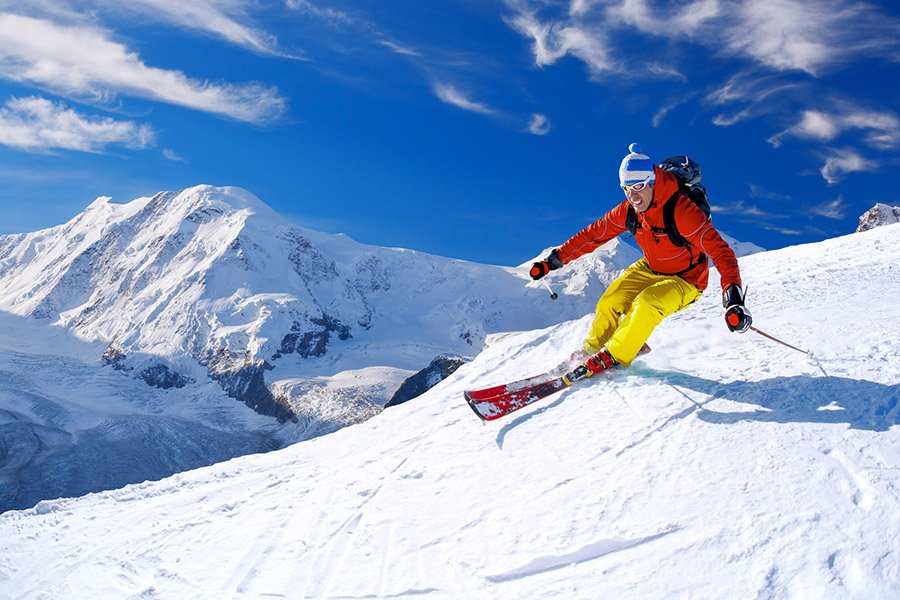 Skier skiing downhill in high mountains against blue sky